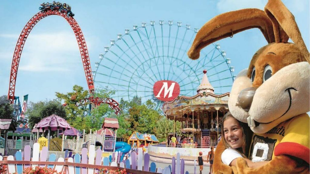 Otto, la mascotte di Mirabilandia, abbraccia una bambina davanti alle principali attrazioni del parco tematico